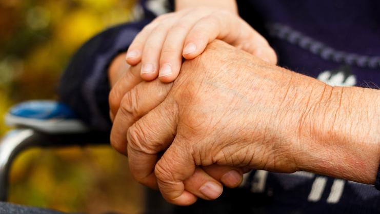 Nahaufnahme zweier Hände, eine ältere und eine jüngere, die sich miteinander halten. Hintergrund unscharf.