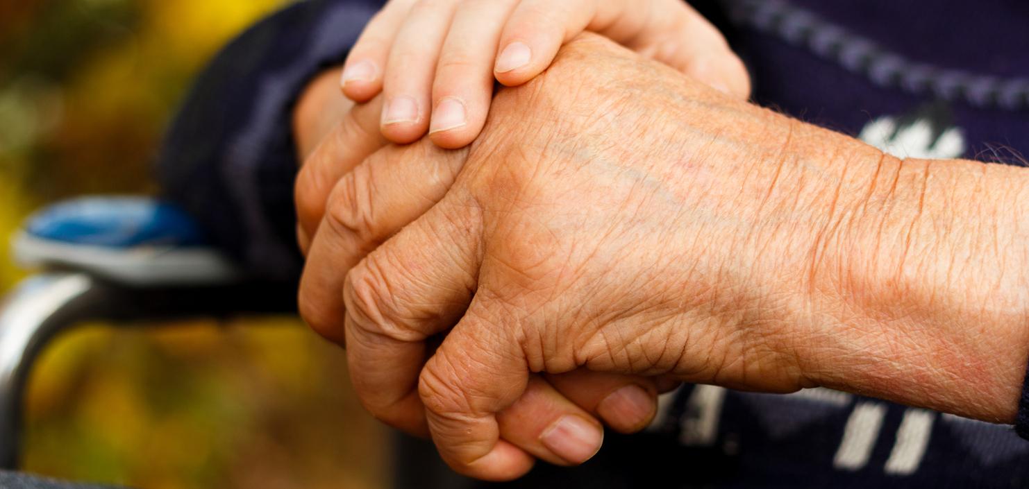 Nahaufnahme zweier Hände, eine ältere und eine jüngere, die sich miteinander halten. Hintergrund unscharf.